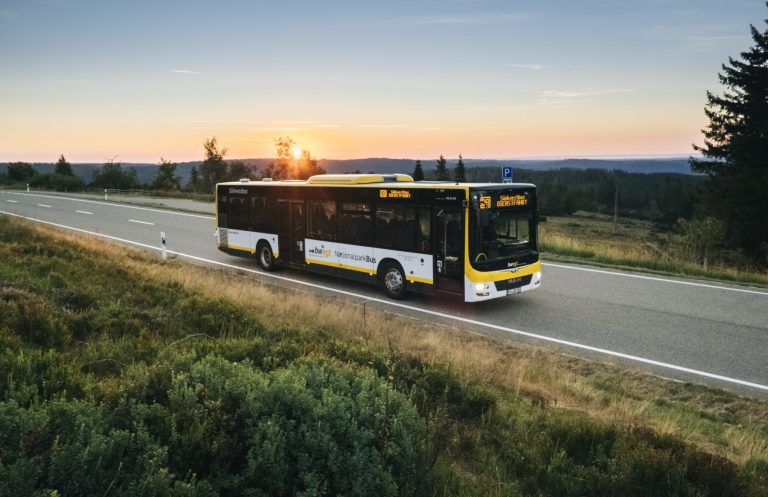 © Schwarzwald Tourismus Gelb-schwarzer Bus fährt auf einer Straße bei Sonnenuntergang durch die Schwarzwaldhöhe.
